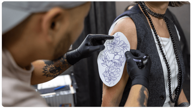 Tattoo artist applying flower stencil to womans arm